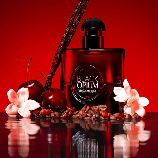 Frasco preto brilhante do perfume YSL Black Opium em cenário elegante com elementos que evocam café, baunilha e flores brancas, sobre fundo escuro e sofisticado.
