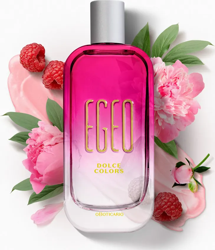 Frasco rosa do perfume Egeo Dolce Colors de O Boticário em close, cercado por flores, framboesas e creme rosa ao fundo.