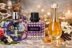Lançamento de perfumes com três frascos em destaque (Floral Street Bridgerton, Valentino roxo e Dior J’adore), cercados por flores, frutas roxas, baunilha e âmbar.