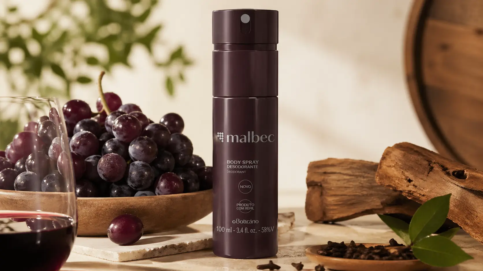 Malbec versões com destaque para o body spray Malbec tradicional de O Boticário em cenário claro com uvas, vinho e madeiras.